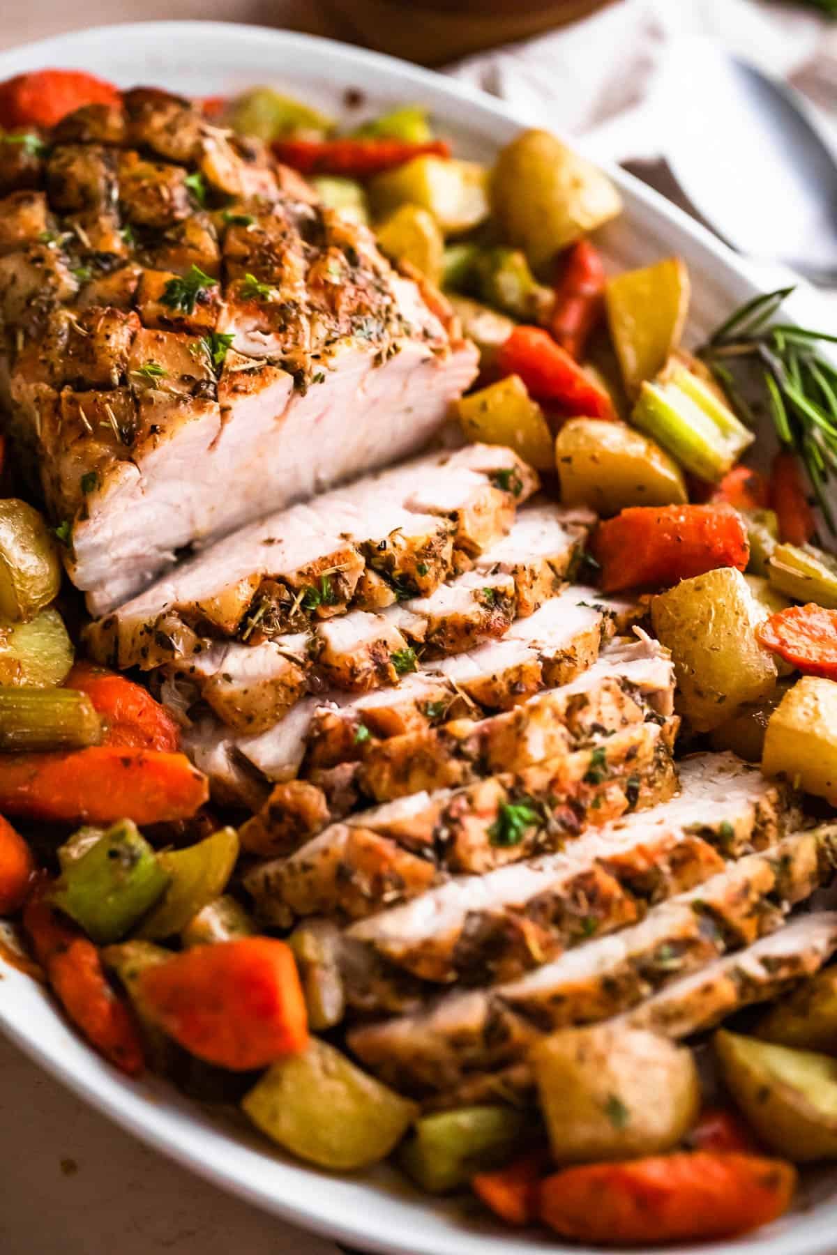 side shot of oval plate with cooked and sliced pork loin roast and roasted vegetables arranged around the roast