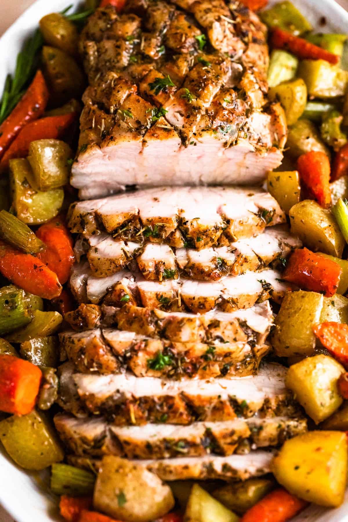 overhead shot of oval plate with cooked and sliced pork loin roast and roasted vegetables arranged around the roast