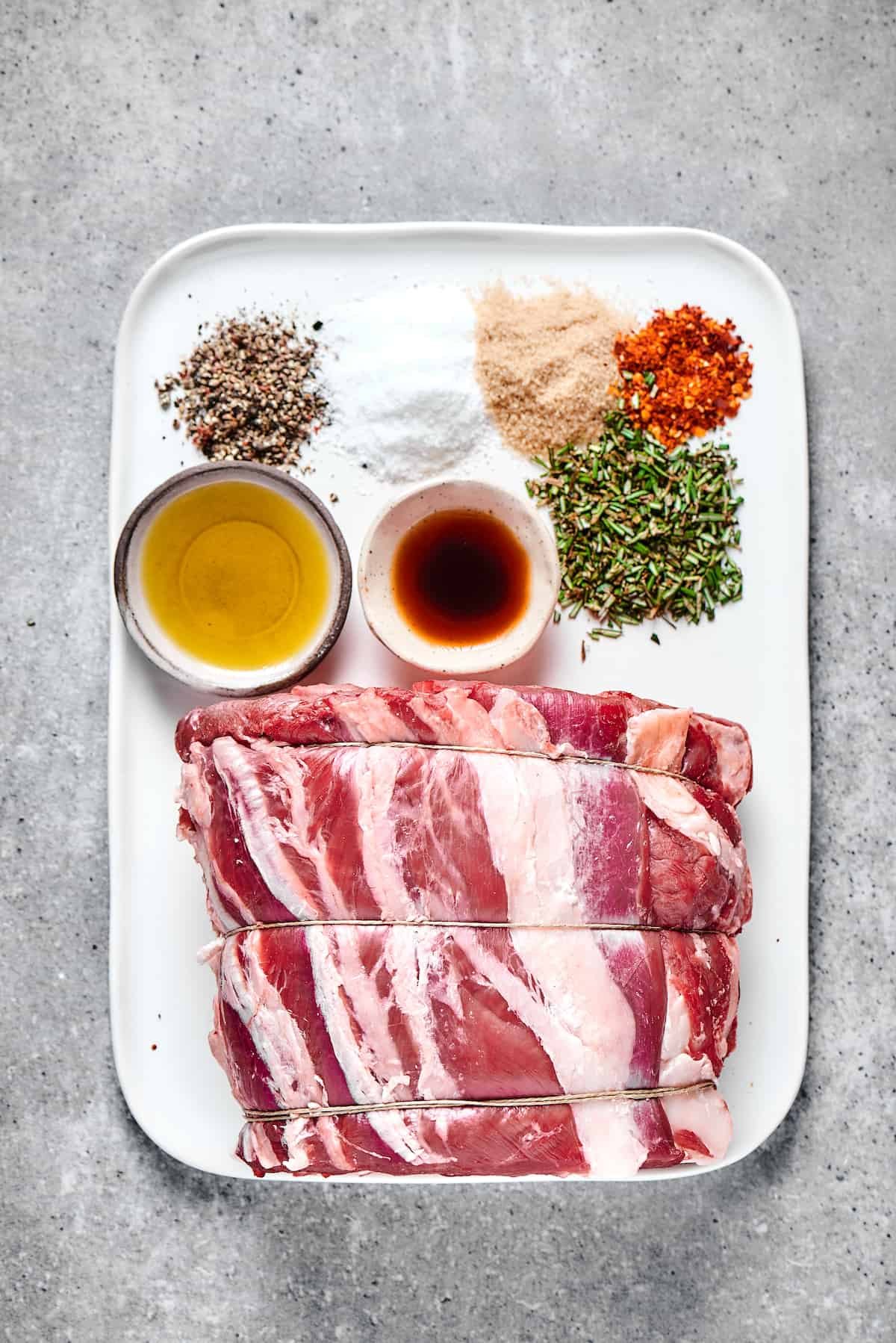 Seasonings, oil, worcestershire sauce, and a tied prime rib roast on an enamel tray.