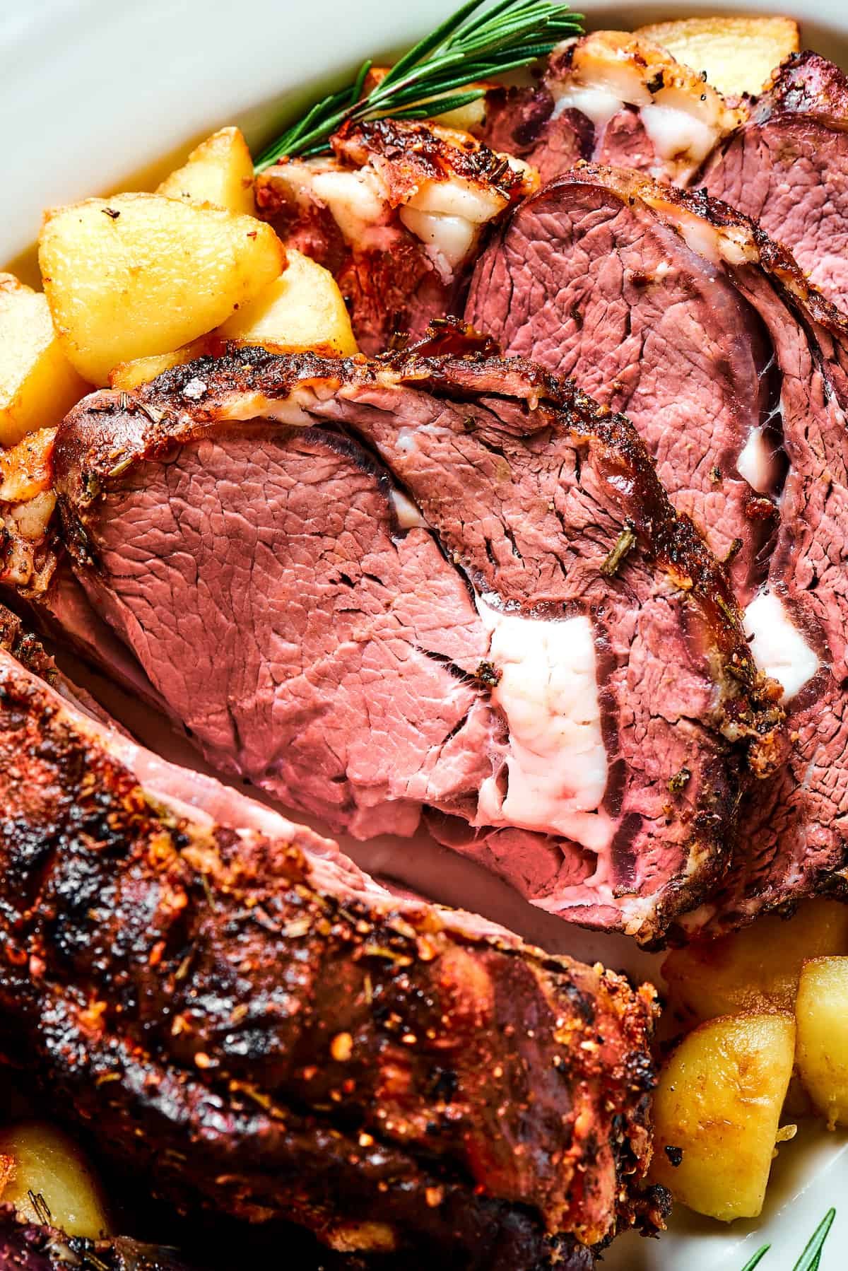 Close-up shot of prime rib, sliced and garnished with herbs.