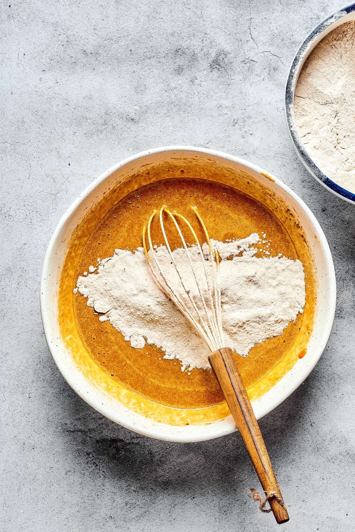 A bowl of pumpkin batter with dry ingredients and a whisk.