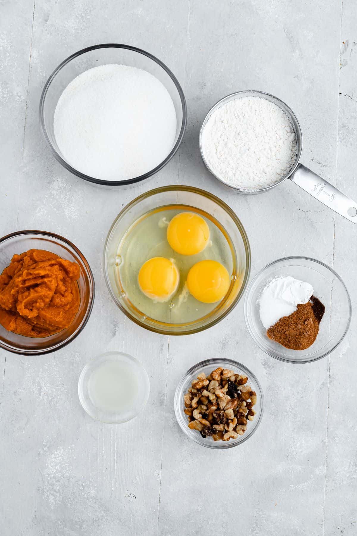Clockwise from top: flour, spices, walnuts, lemon juice, pumpkin puree, sugar. Center: 3 eggs.