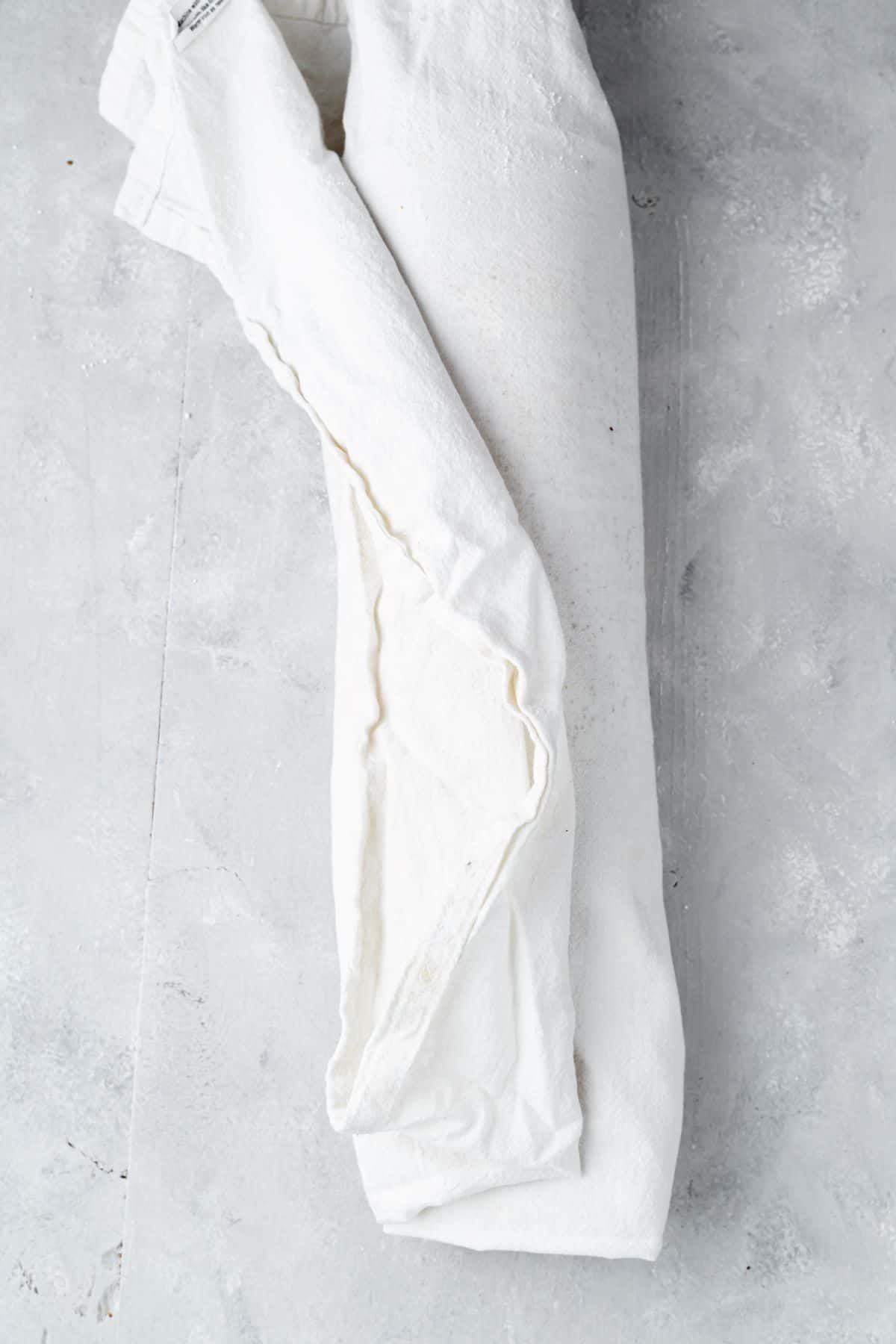The pumpkin roll cake rolled up tightly in a linen tea towel.