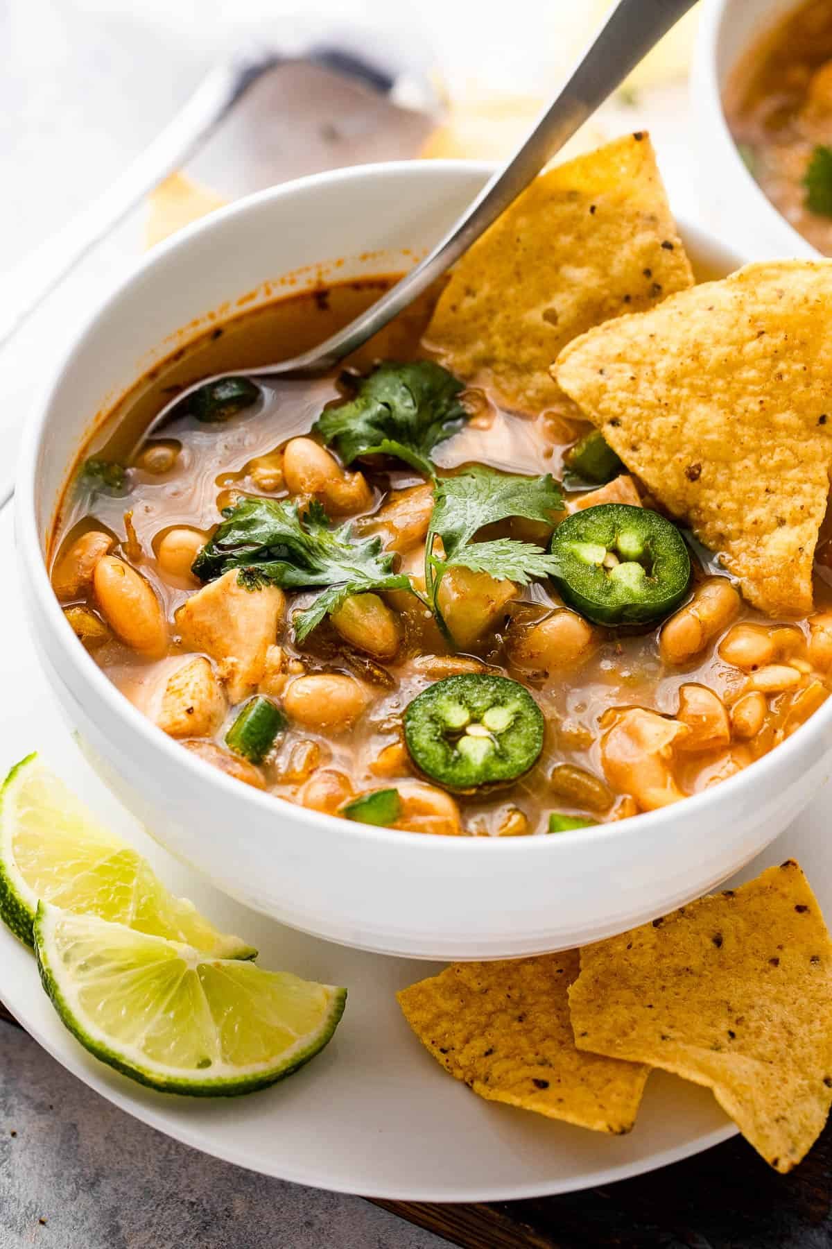 side shot of a chicken chili in a bowl topped with jalapenos and tortilla chips