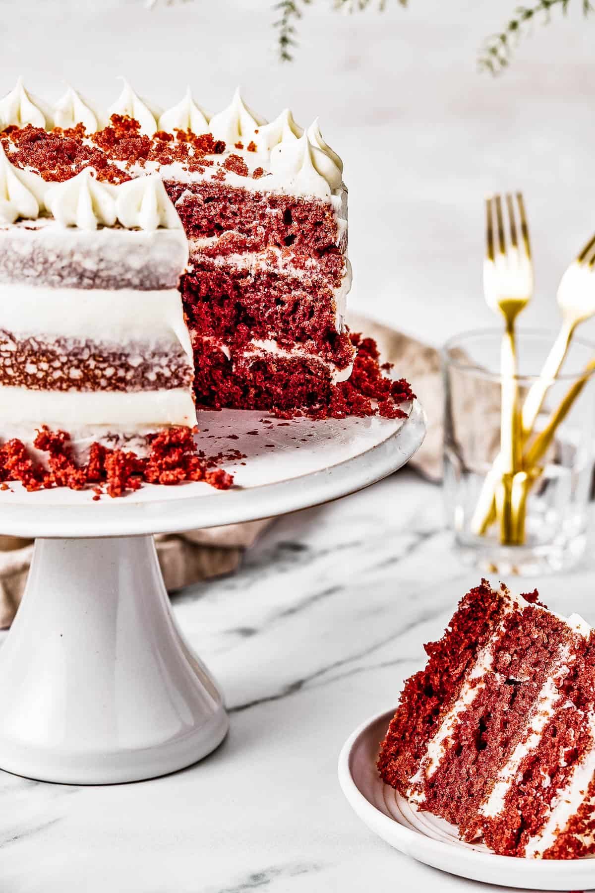 A cake on a cake stand, with a slice cut out and set on a small plate nearby.