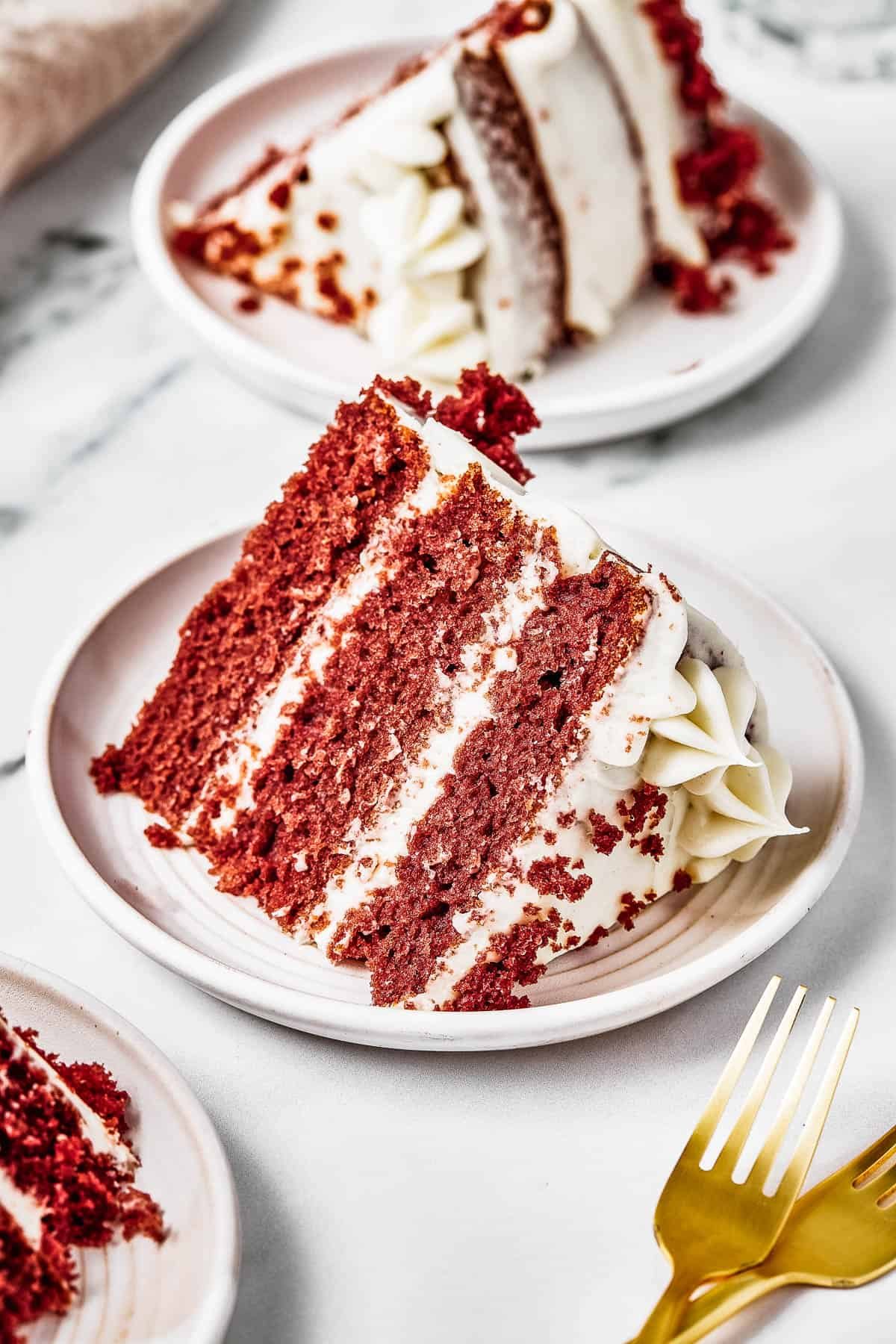 A slice of layer cake on a small plate, with golden forks next to it on the table.