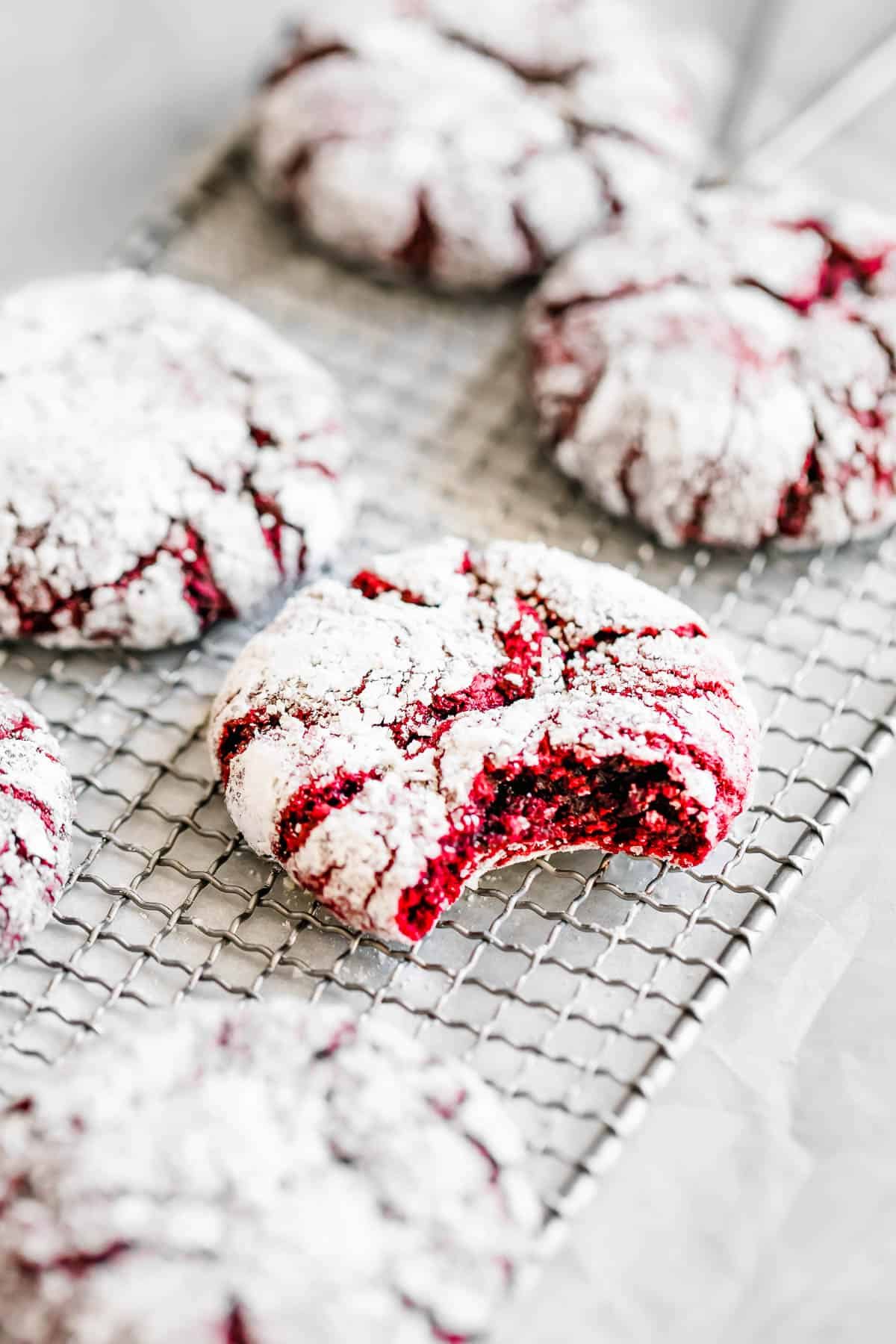 Six Red Velvet Crinkle Cookies on a Wire Cooling Rack with One Cookie Missing a Bite