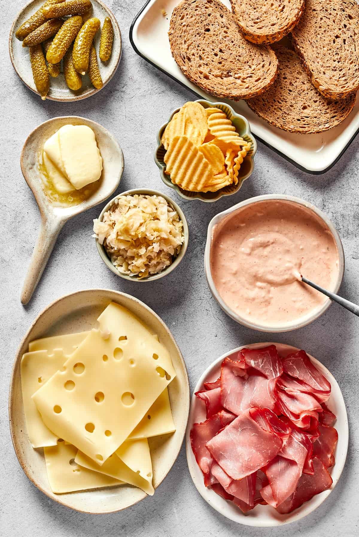Pickles, bread, potato chips, russian dressing, sliced corned beef, swiss cheese, sauerkraut, and butter.