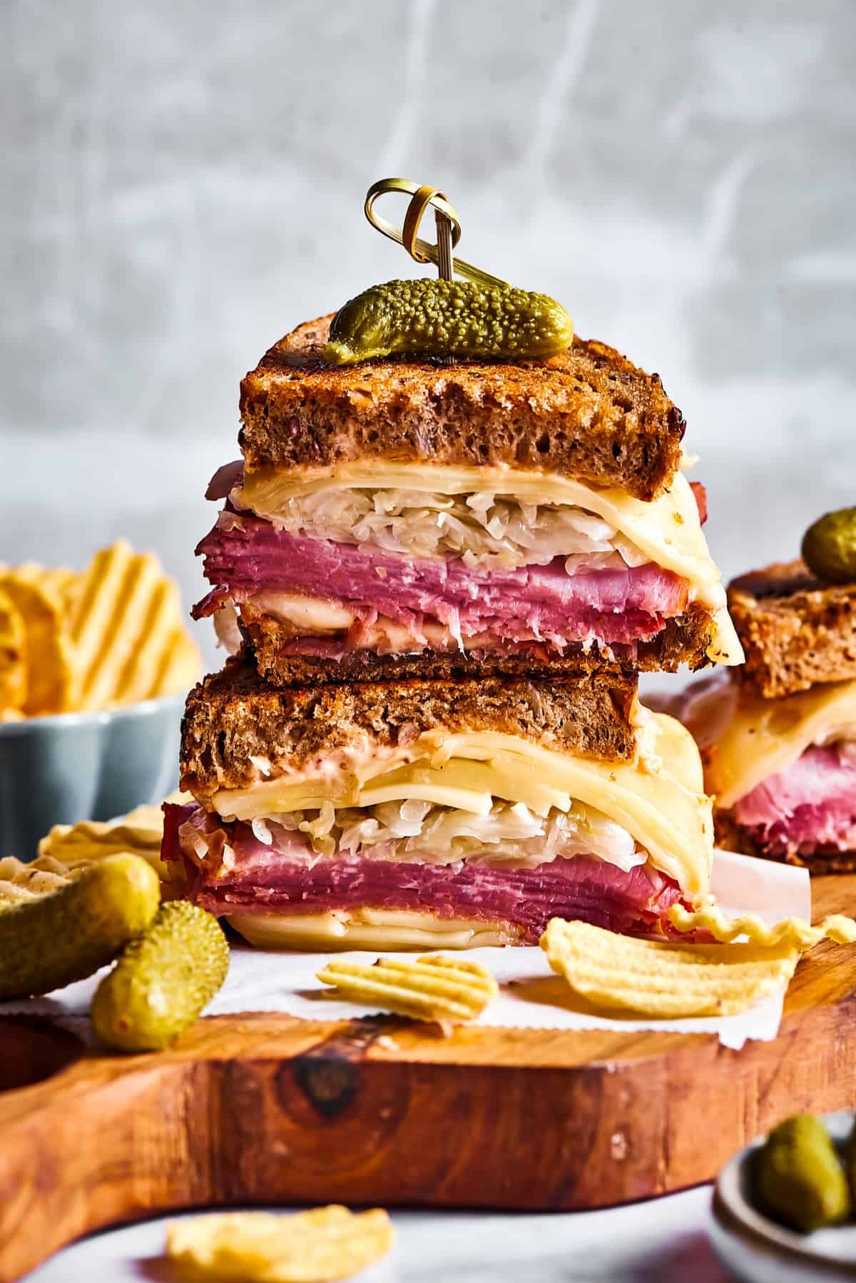Sandwiches, Russian dressing, chips, and pickles on a cutting board.
