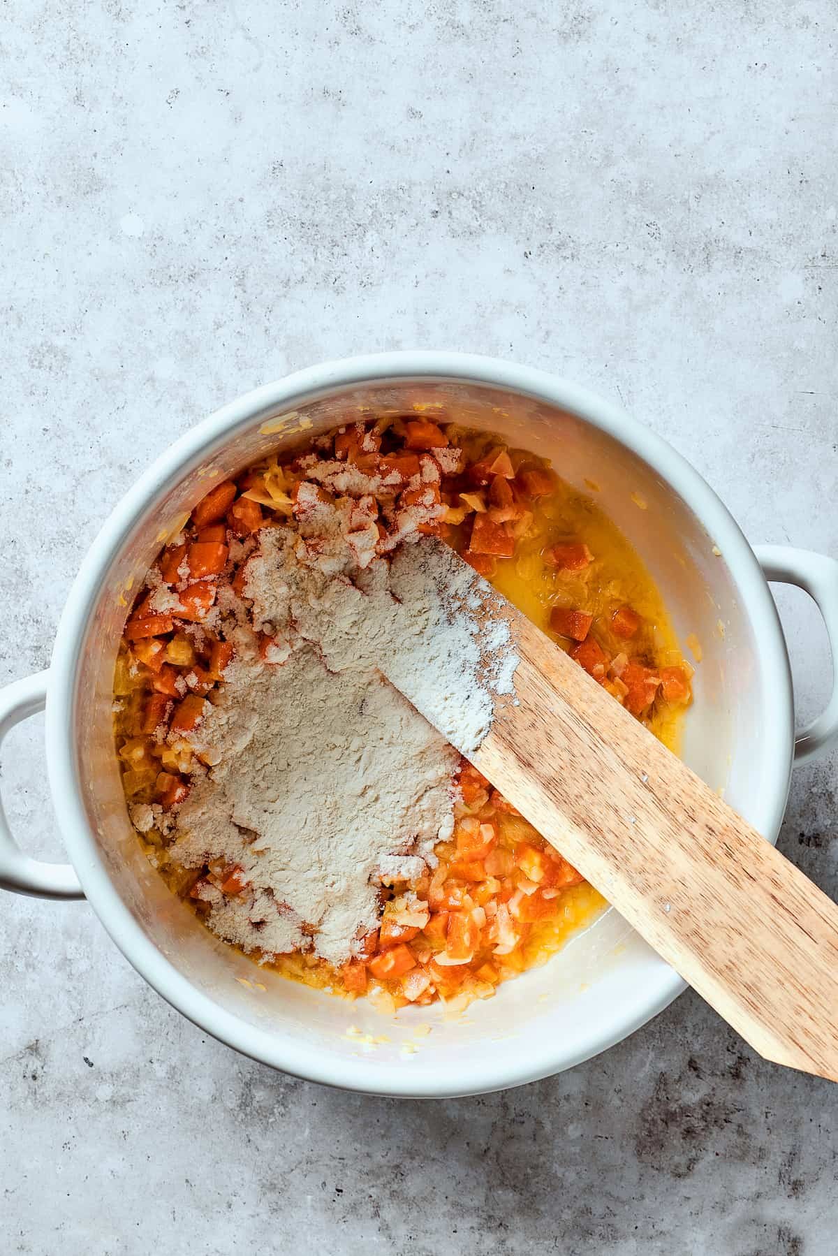 Adding flour to cooked veggies in a Dutch oven.