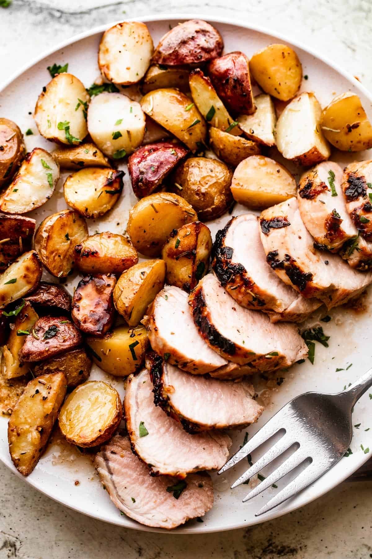 overhead shot of a serving plate with sliced roast pork tenderloin served with colored baby potatoes
