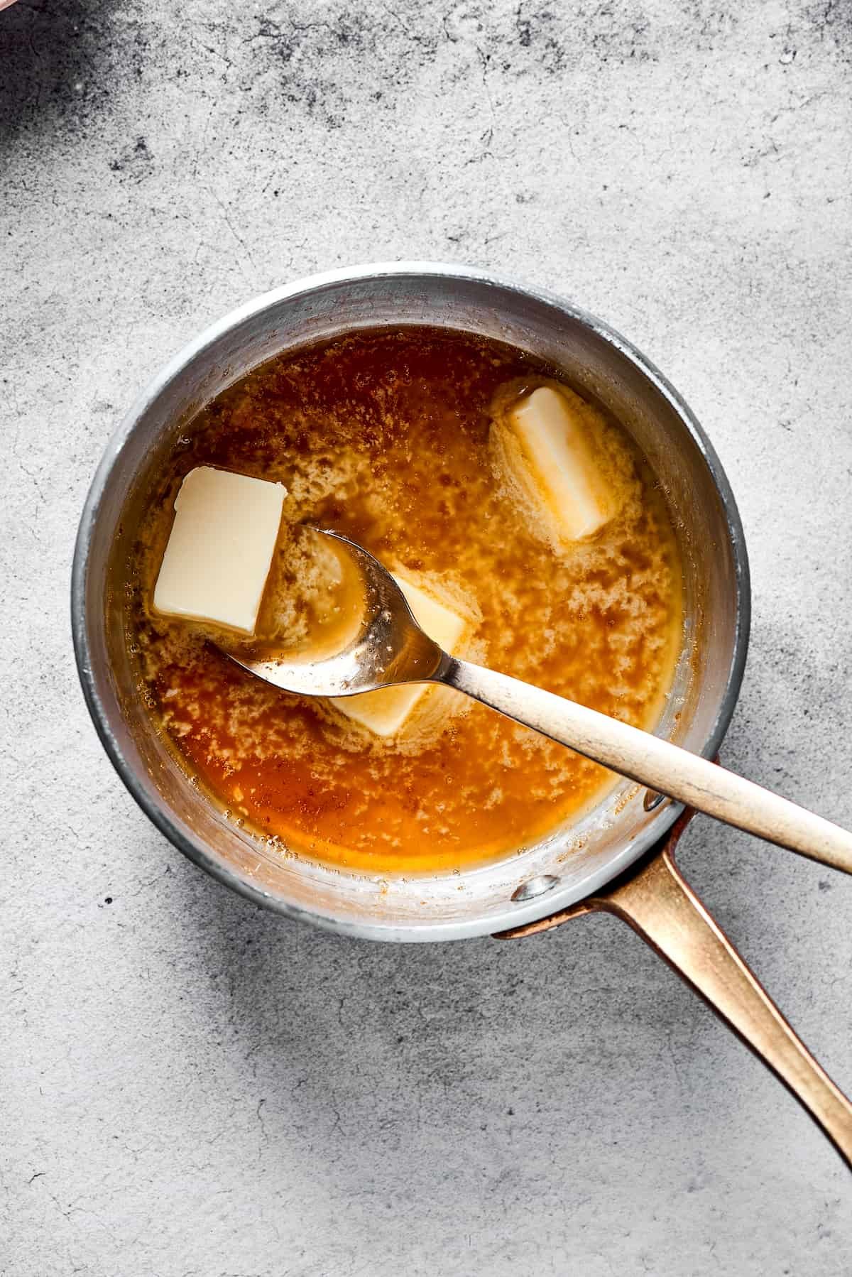 Stirring butter into a small saucepan of maple glaze.
