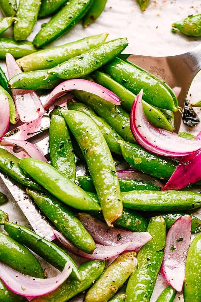 scooping up roasted snap peas from a baking sheet