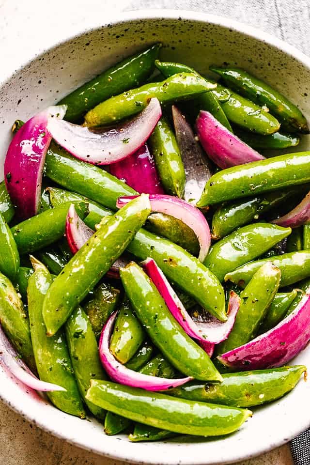roasted sugar snap peas with red onions served in a cream bowl