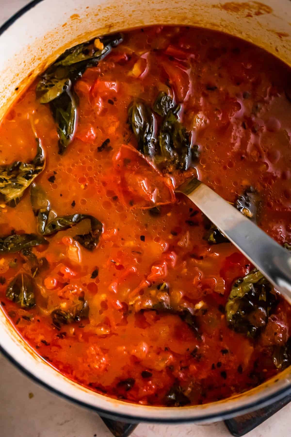 overhead shot of a pot with tomato soup and basil leaves.