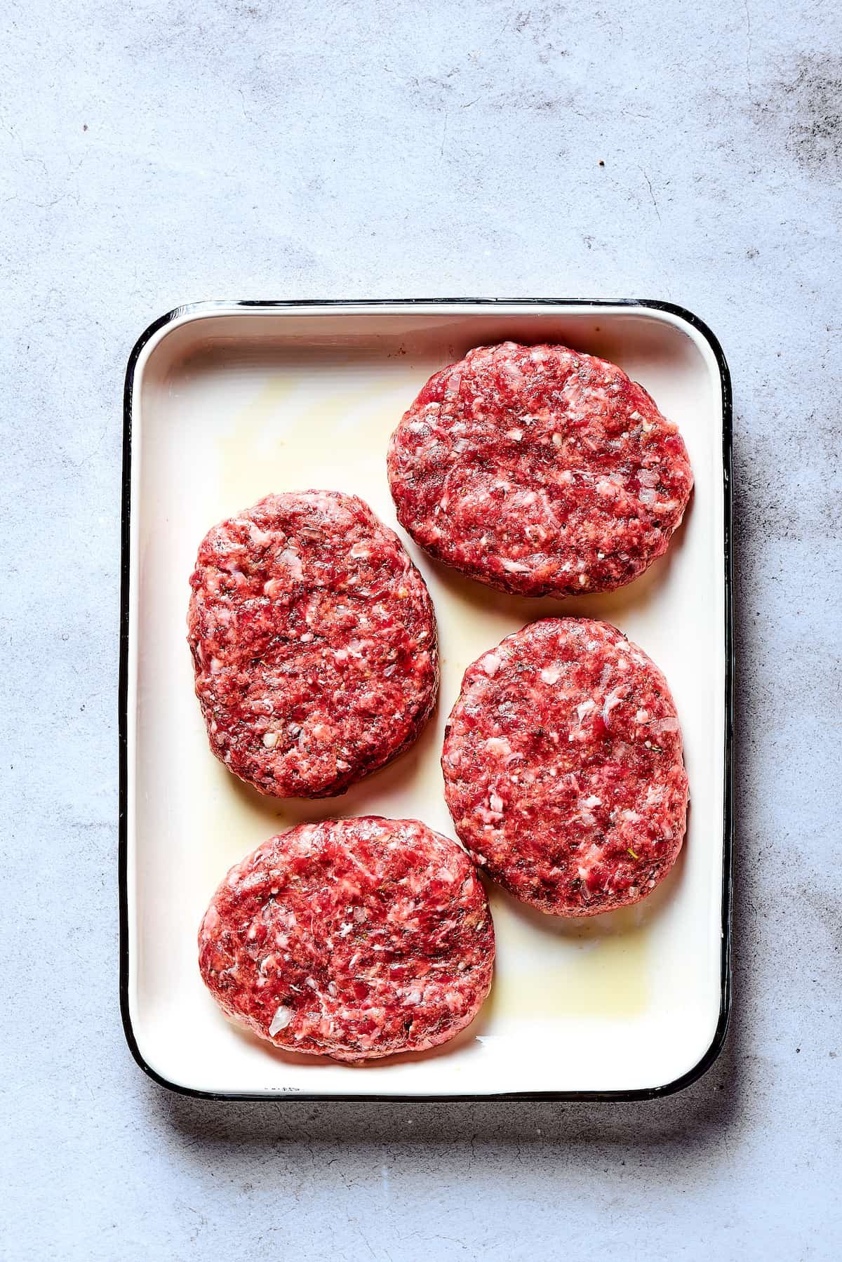 Shaped beef patties on an enamel tray.