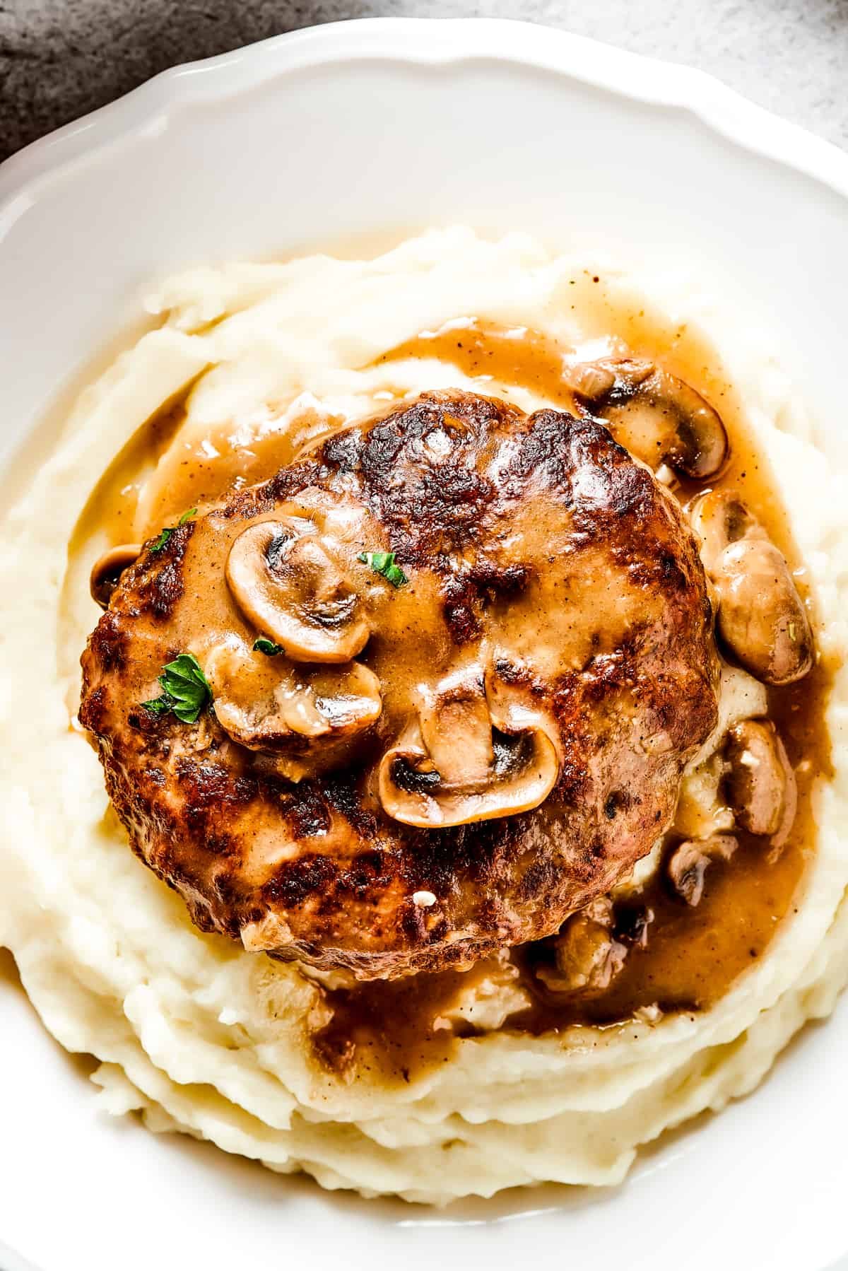 Salisbury steak with mushroom gravy served on a dinner plate over mashed potatoes.