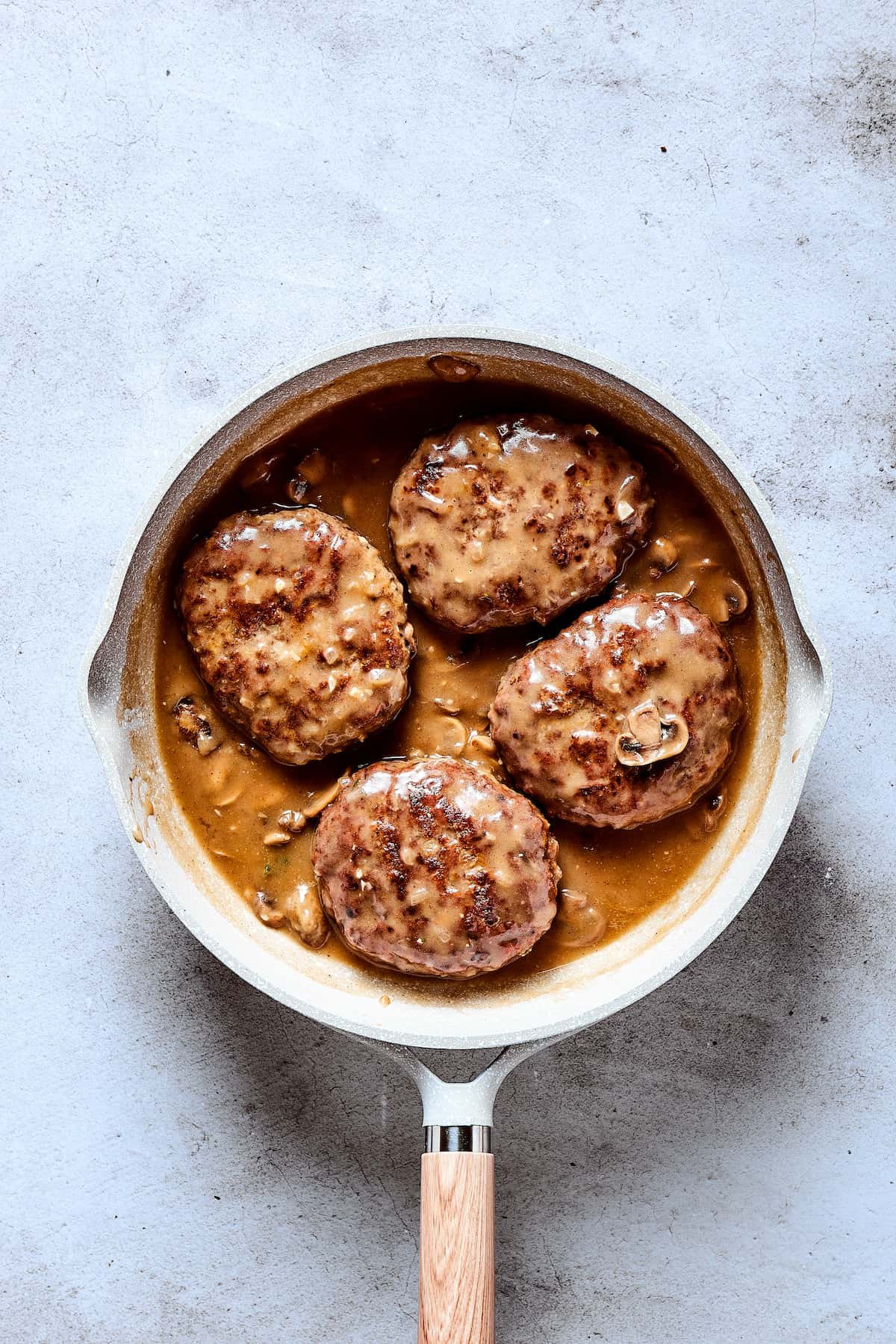 A finished skillet of beef patties with gravy.