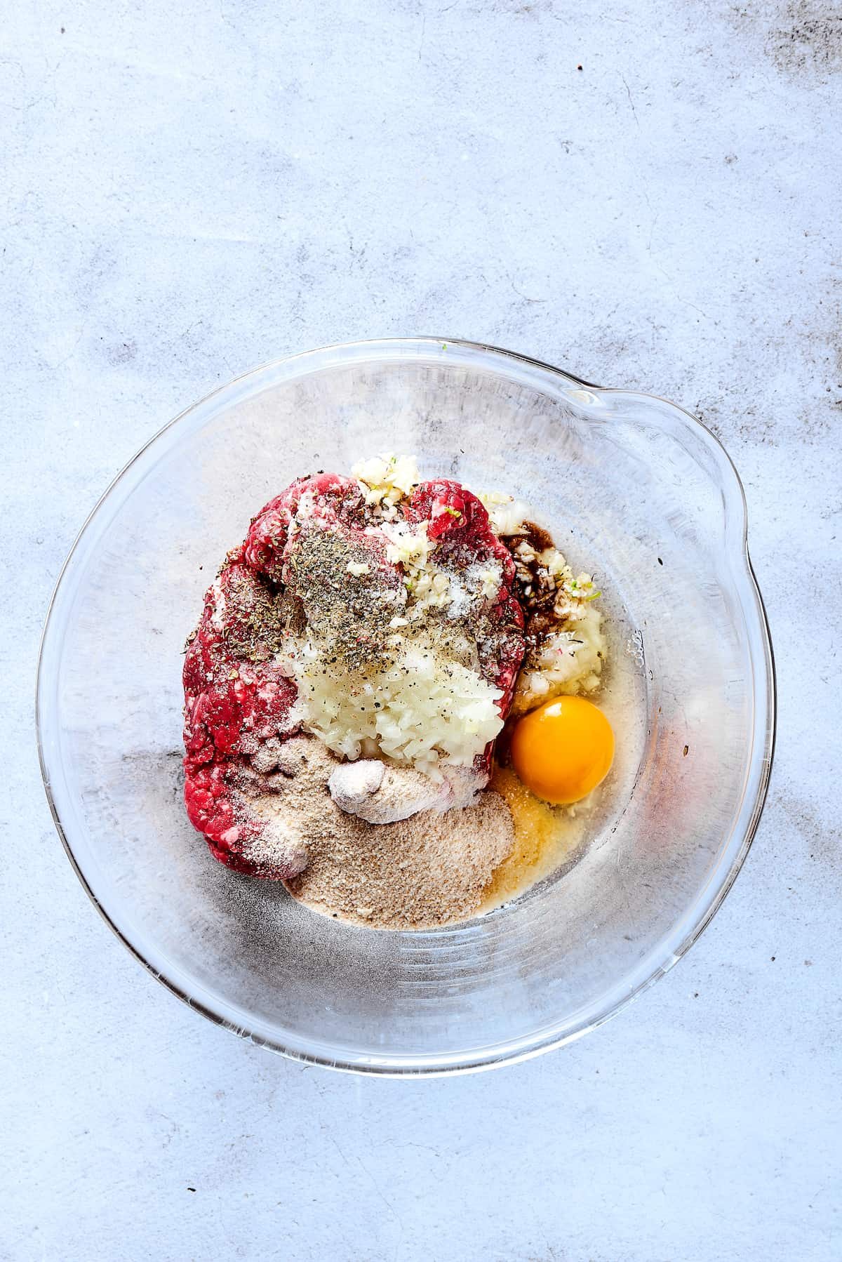 Ground beef, eggs, and other ingredients in a glass dish.
