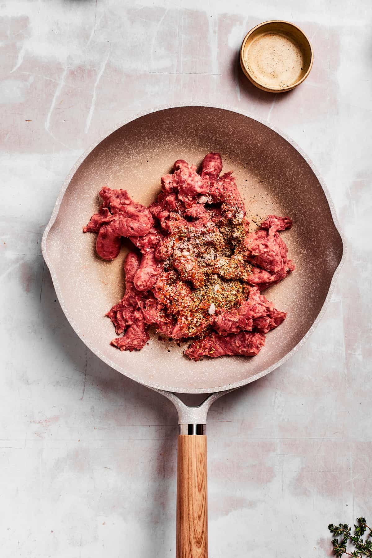 Sausage and herbs are added to a pan.