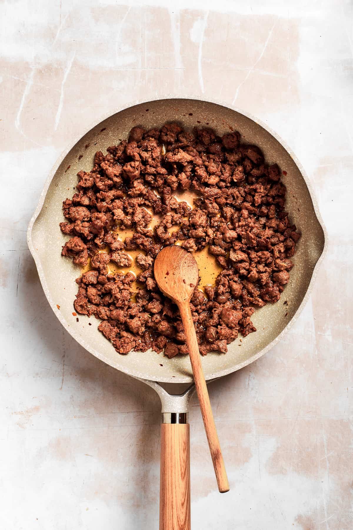 A wooden spoon stirs the pan of sausage.