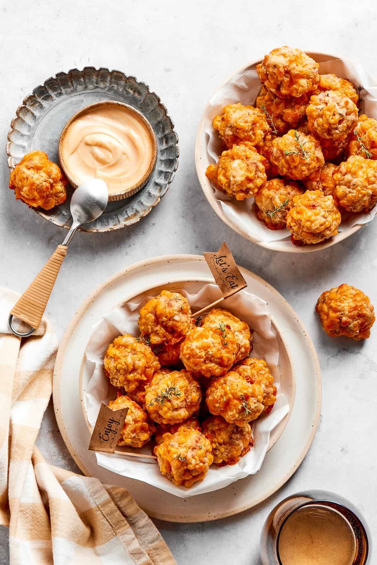 Two bowls of sausage balls and a bowl of dip and a spoon.