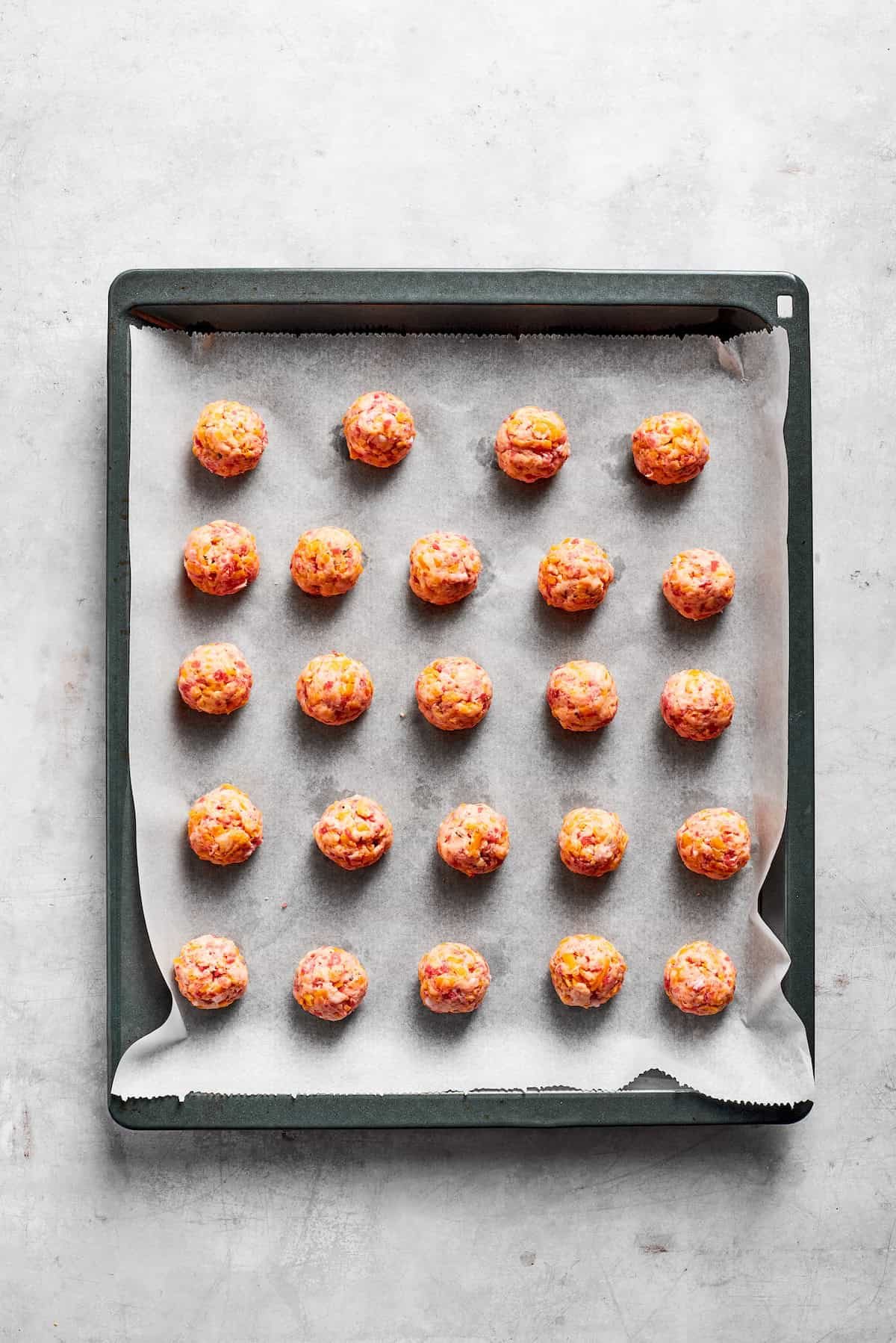 A lined baking tray with sausage balls.