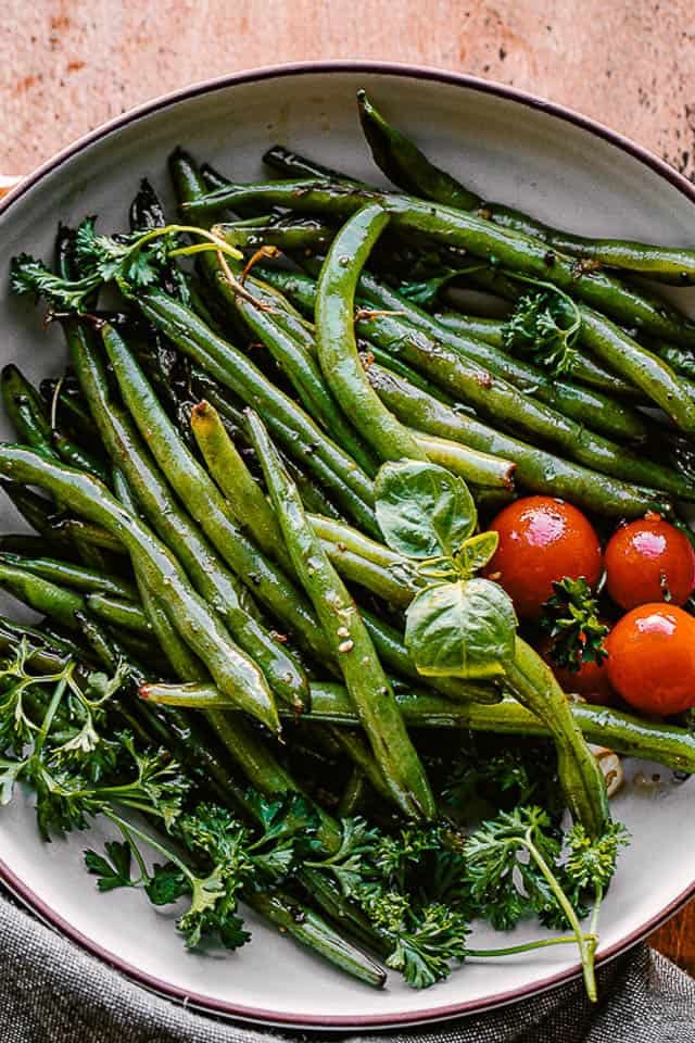 cooked green beans served in a bowl with fresh basil and cherry tomatoes