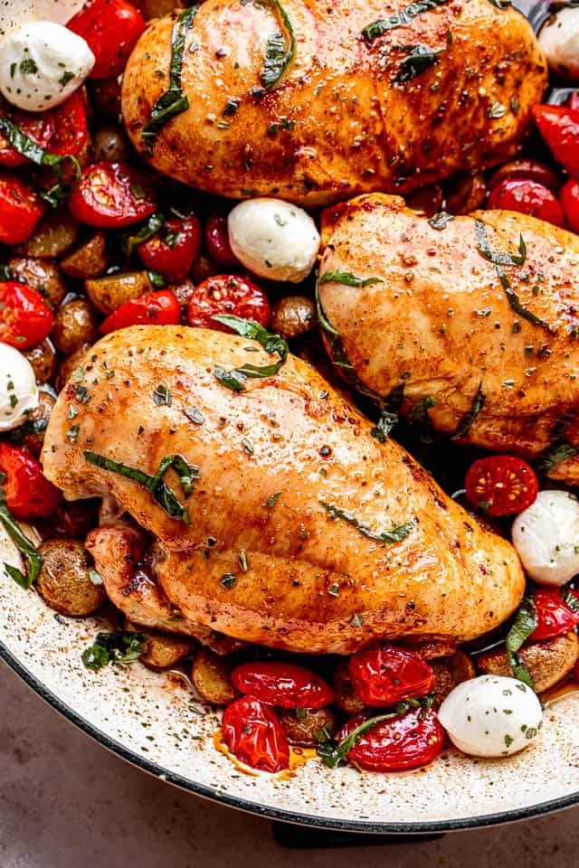 top close up shot of chicken breasts brushed with balsamic vinegar and set next to cherry tomatoes, mozzarella cheese balls, and garnish of basil
