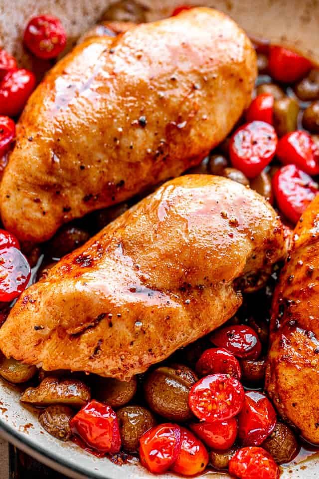 chicken breasts set over a bed of cherry tomatoes and small potatoes