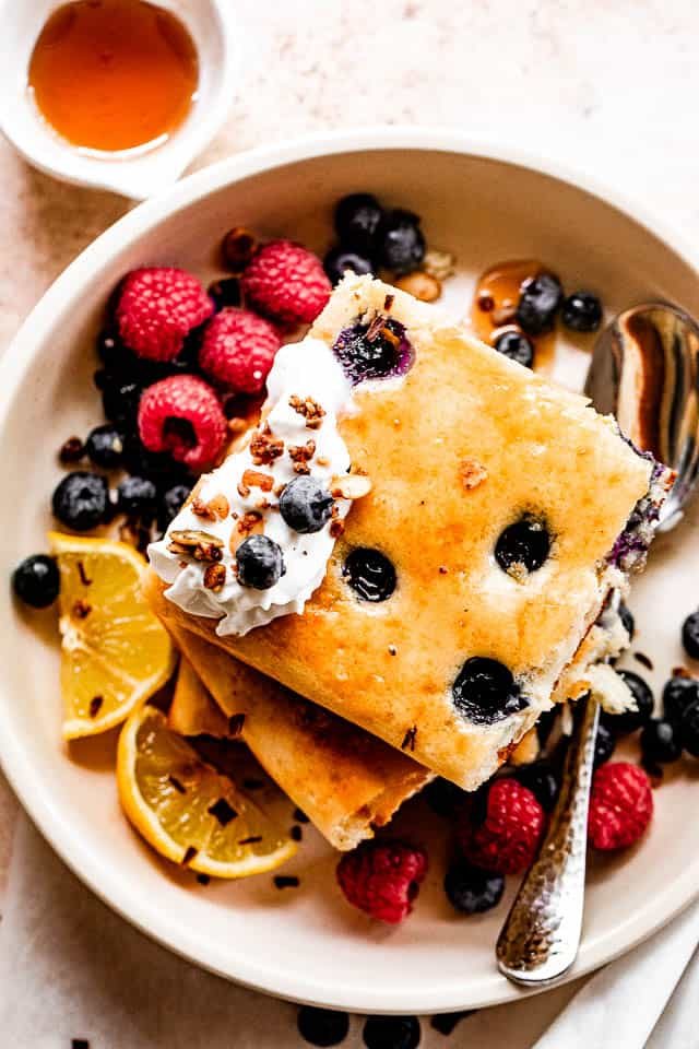 top shot of squared pancakes topped with whipped cream, berries around the pancakes, and maple syrup to the side