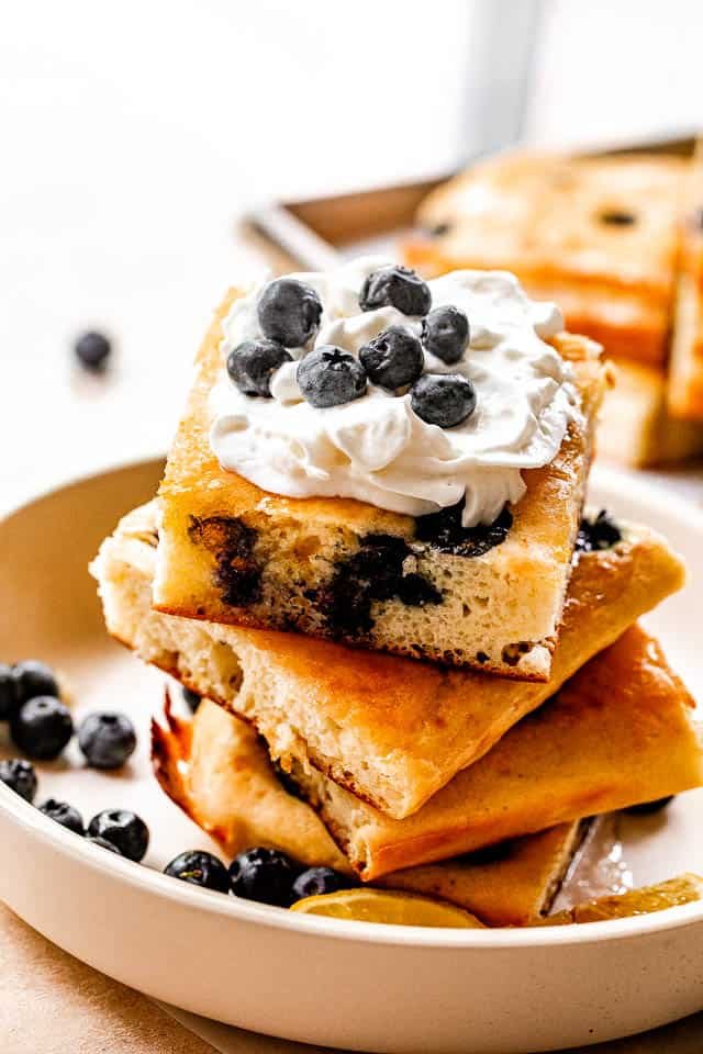 side shot of stacked sheet pan pancakes topped with whipped cream and blueberries