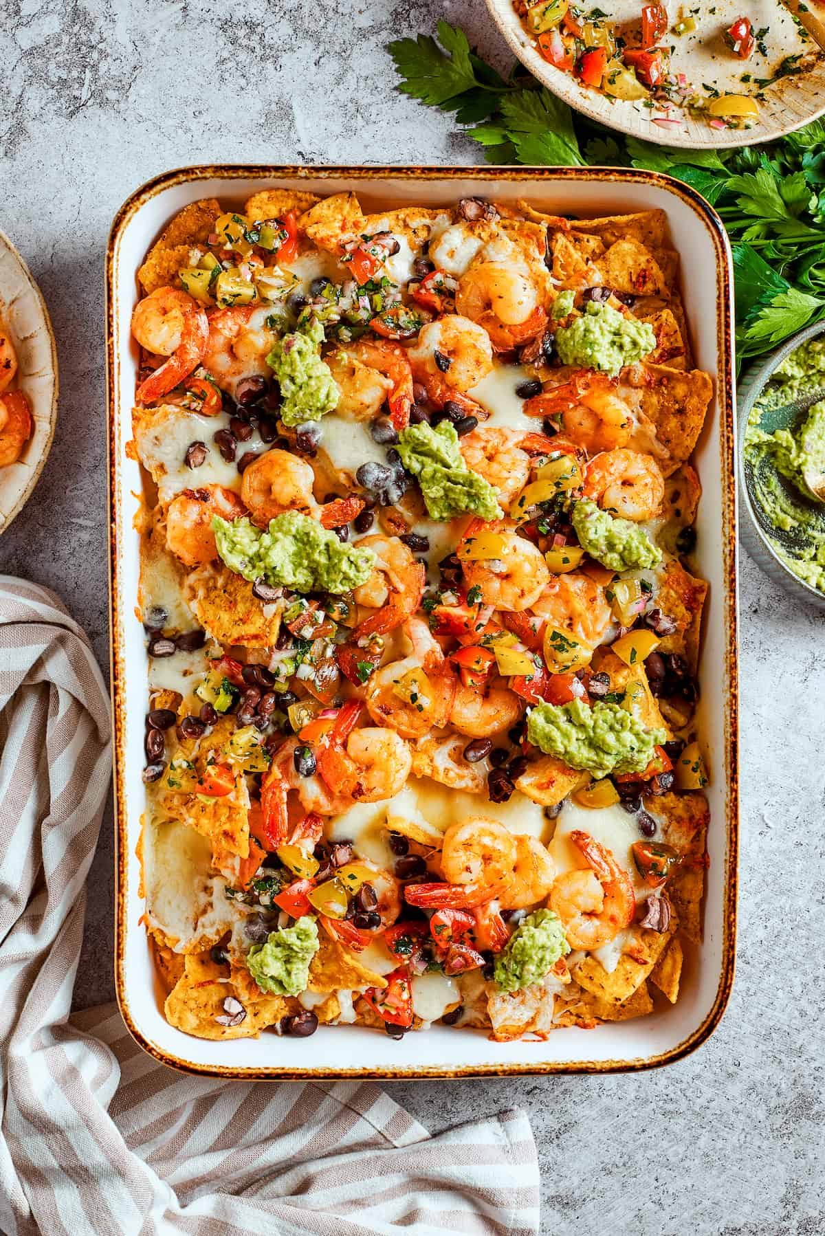 Guacamole is dolloped onto the tray of shrimp nachos.