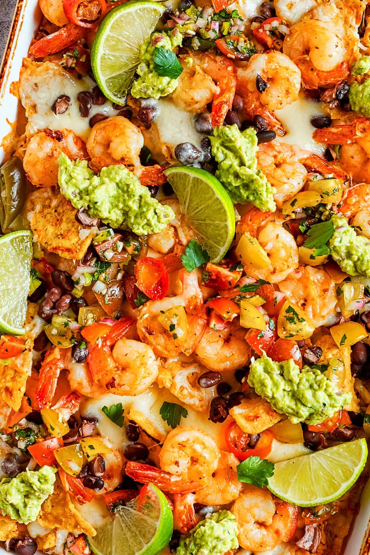 Tortilla chips topped with shrimp, cheese, black beans, tomatoes, and a garnish of guacamole and slices of lime.