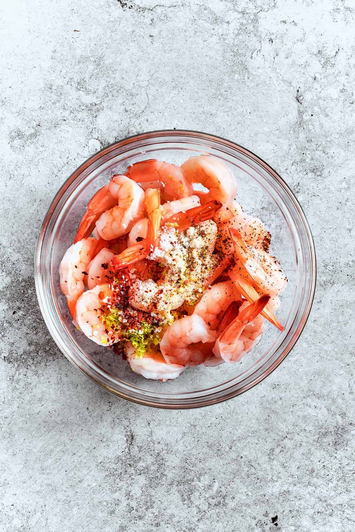 Seasonings are added to shrimp in a bowl.