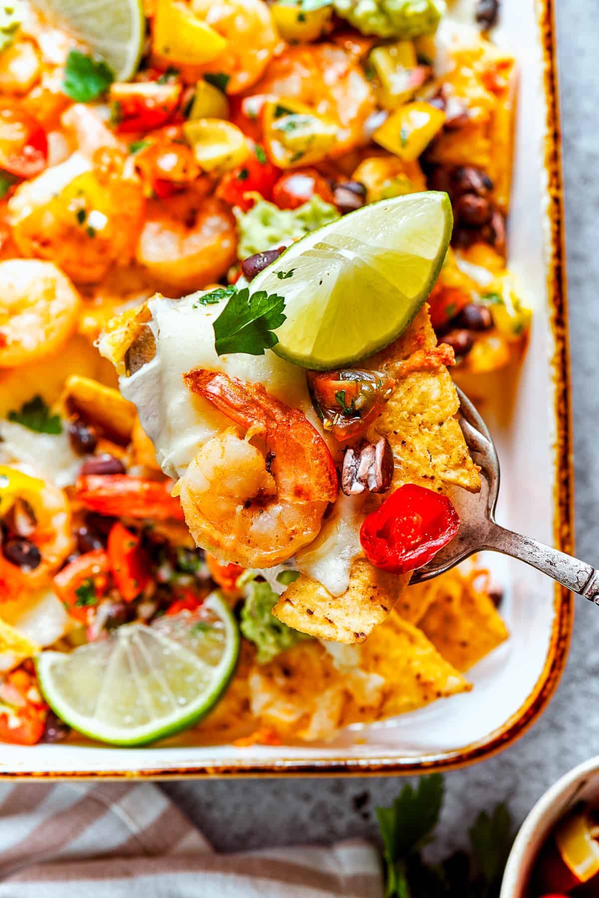 A spoon lifts out nachos from a baking dish.
