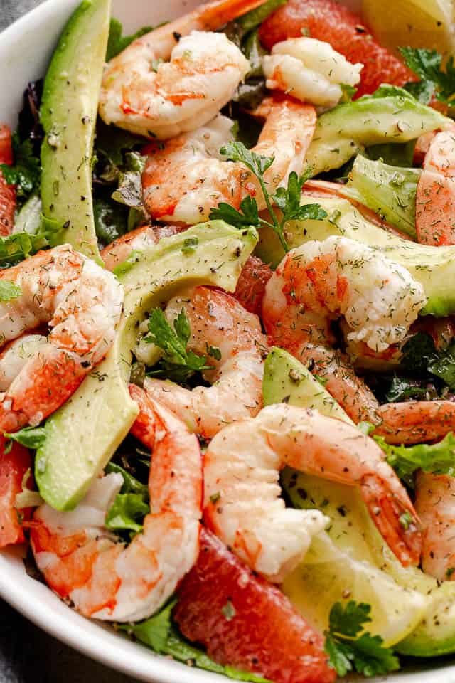 cooked shrimp, avocado slices, and salad greens tossed together in a white serving bowl