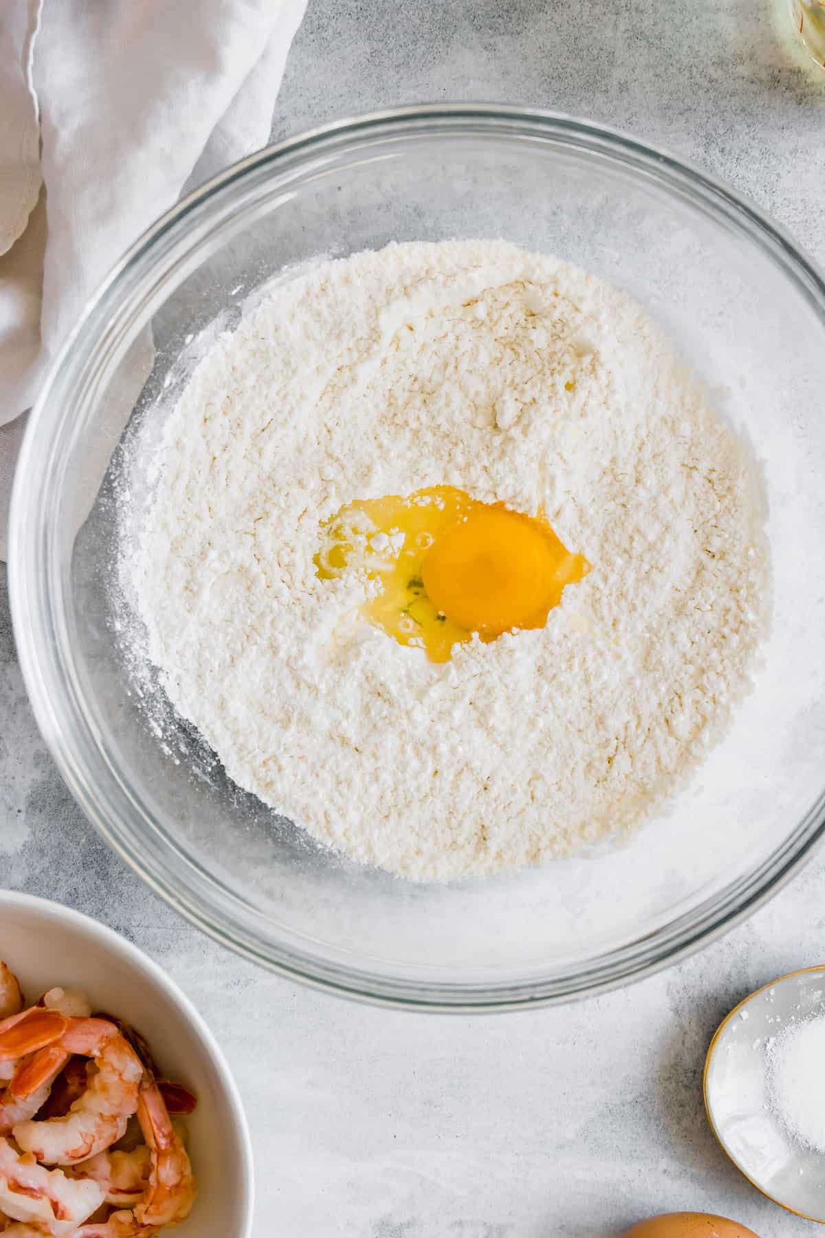 A Glass Bowl Containing the Dry Tempura Ingredients with a Cracked Egg in the Center
