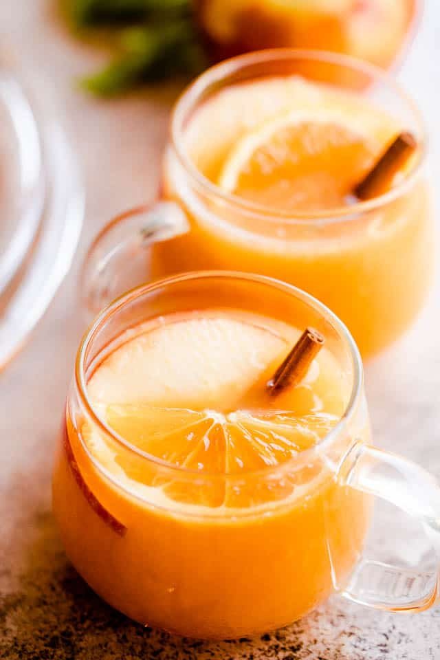 side shot of two glass mugs filled with apple cider punch and served with cinnamon sticks inside
