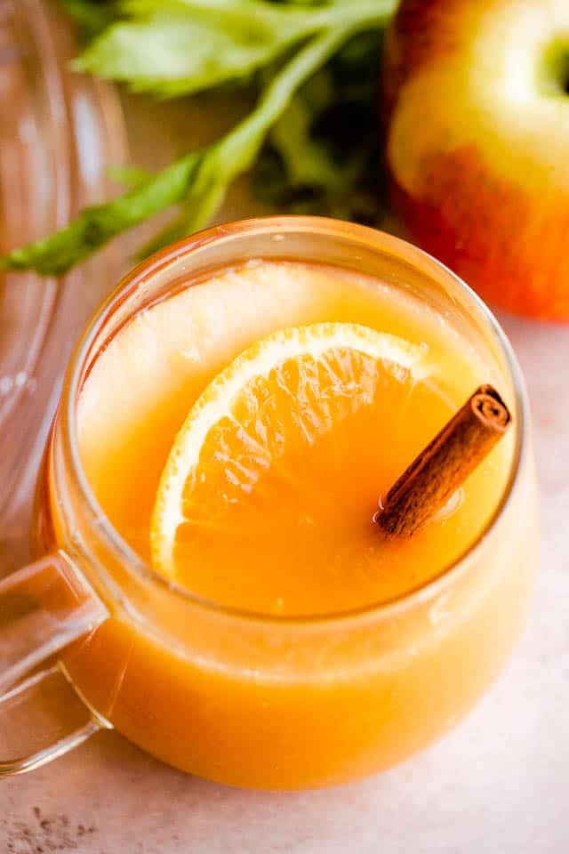 side shot of two glass mugs filled with apple cider punch and served with cinnamon sticks, apple slices, and orange slices inside