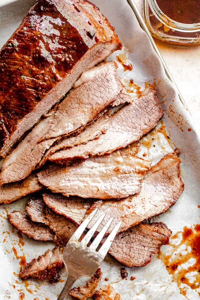 top view of sliced beef brisket with a silver fork placed at the bottom slice and a jar with barbecue sauce to the side