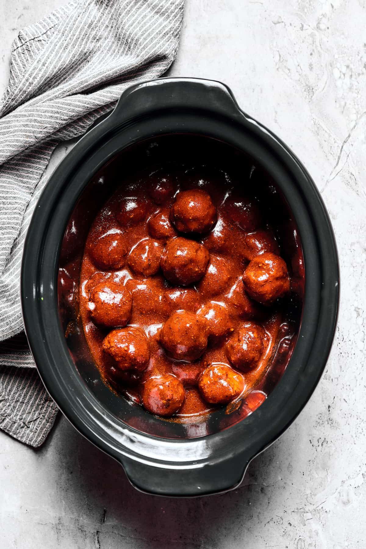 A slow cooker viewed from the top, filled with grape jelly meatballs.