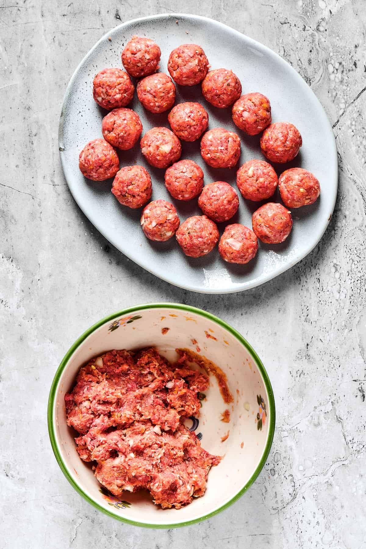 A bowl of meatloaf mixture next to a platter of shaped meatballs.