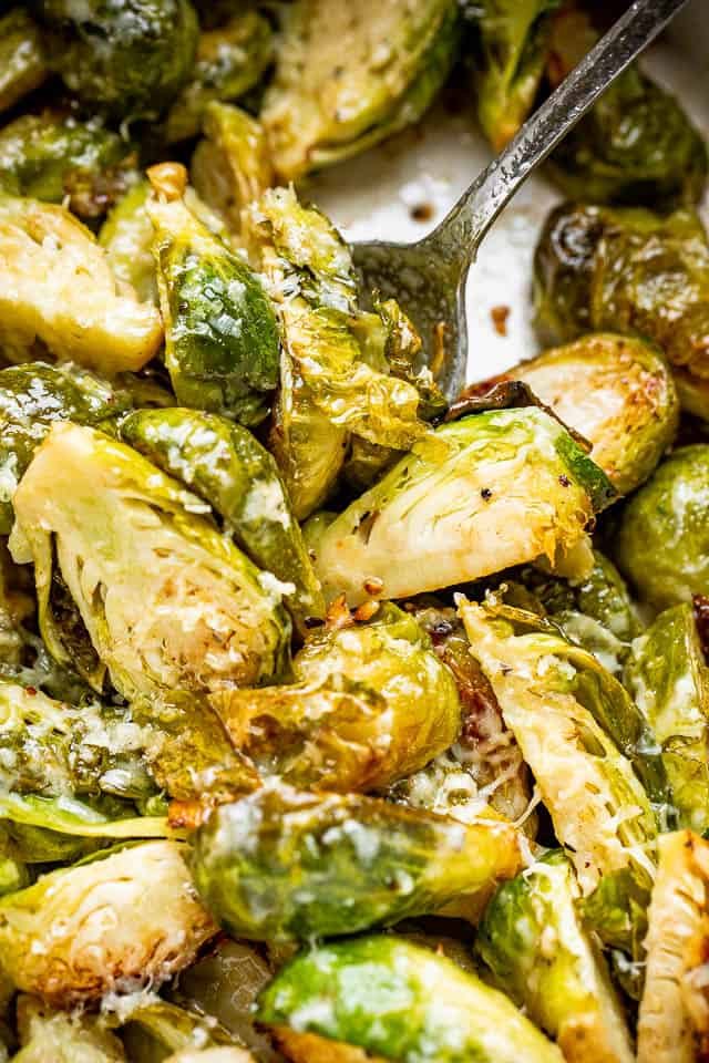 Halved, cooked brussels sprouts in the slow cooker. A serving spoon is stuck into the sprouts.