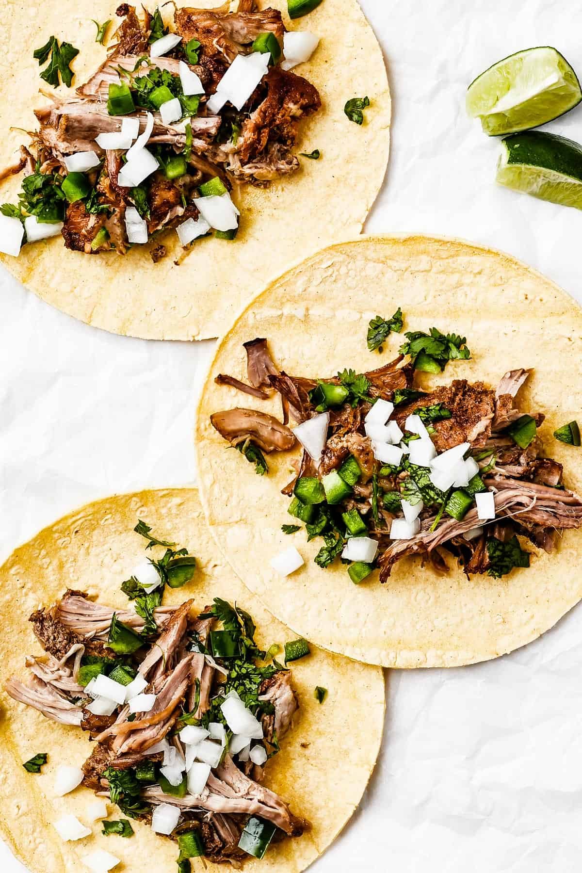 Three tortillas, each with shredded pork and toppings in the center.
