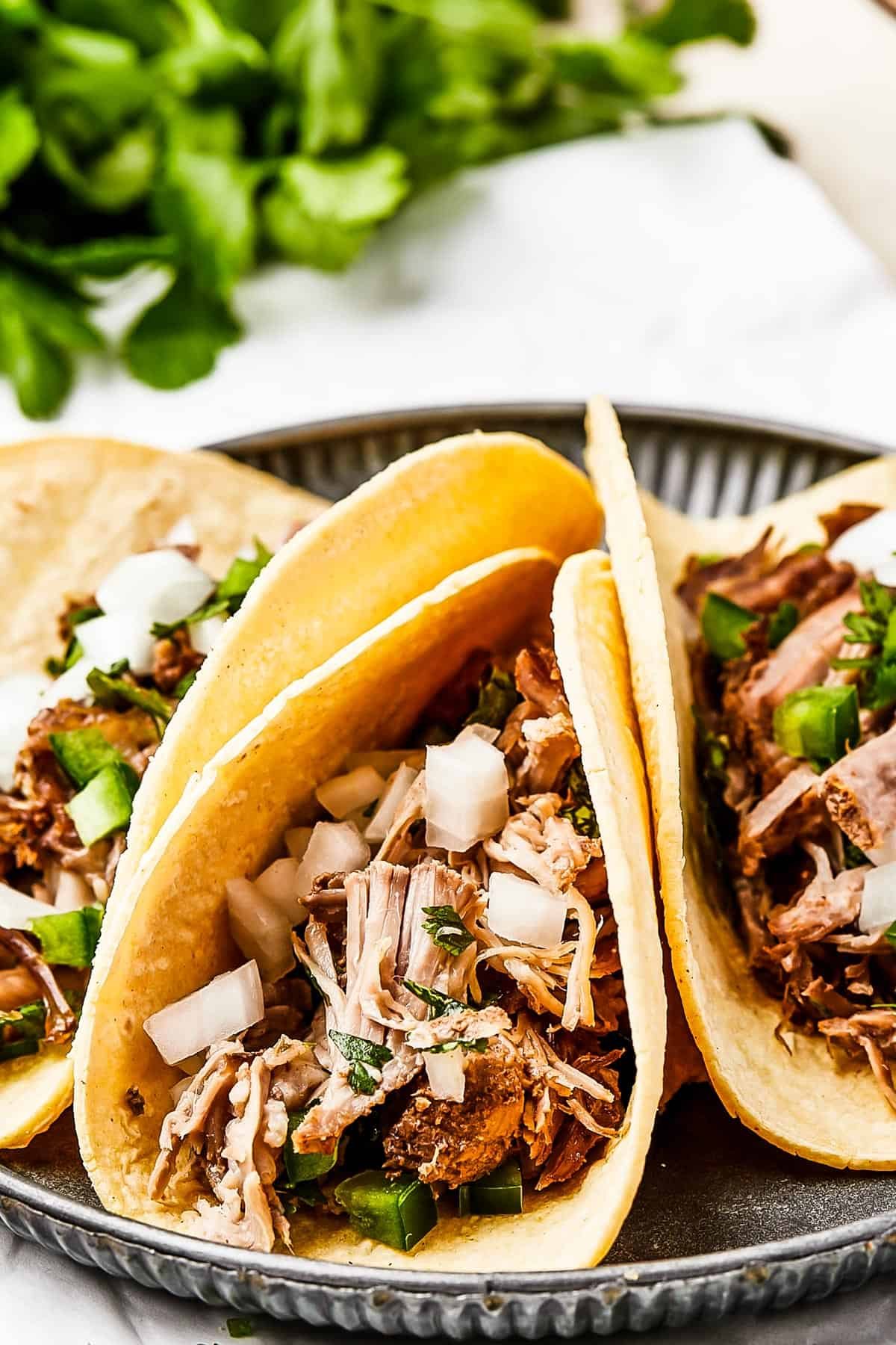 Close-up shot of three pork tacos with onion and herbs.