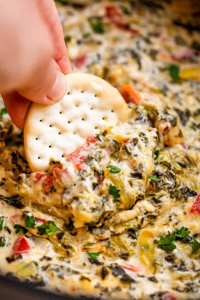 dipping a round cracker in spinach artichoke dip