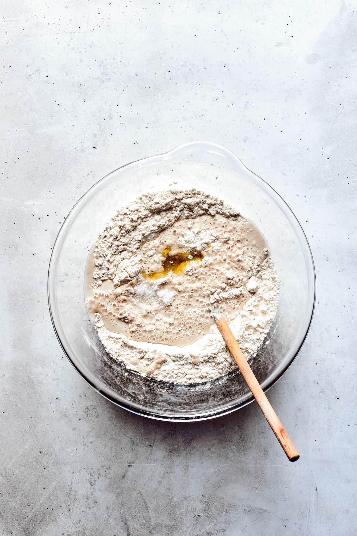 A glass bowl of soft pretzel dough with a wooden spoon.
