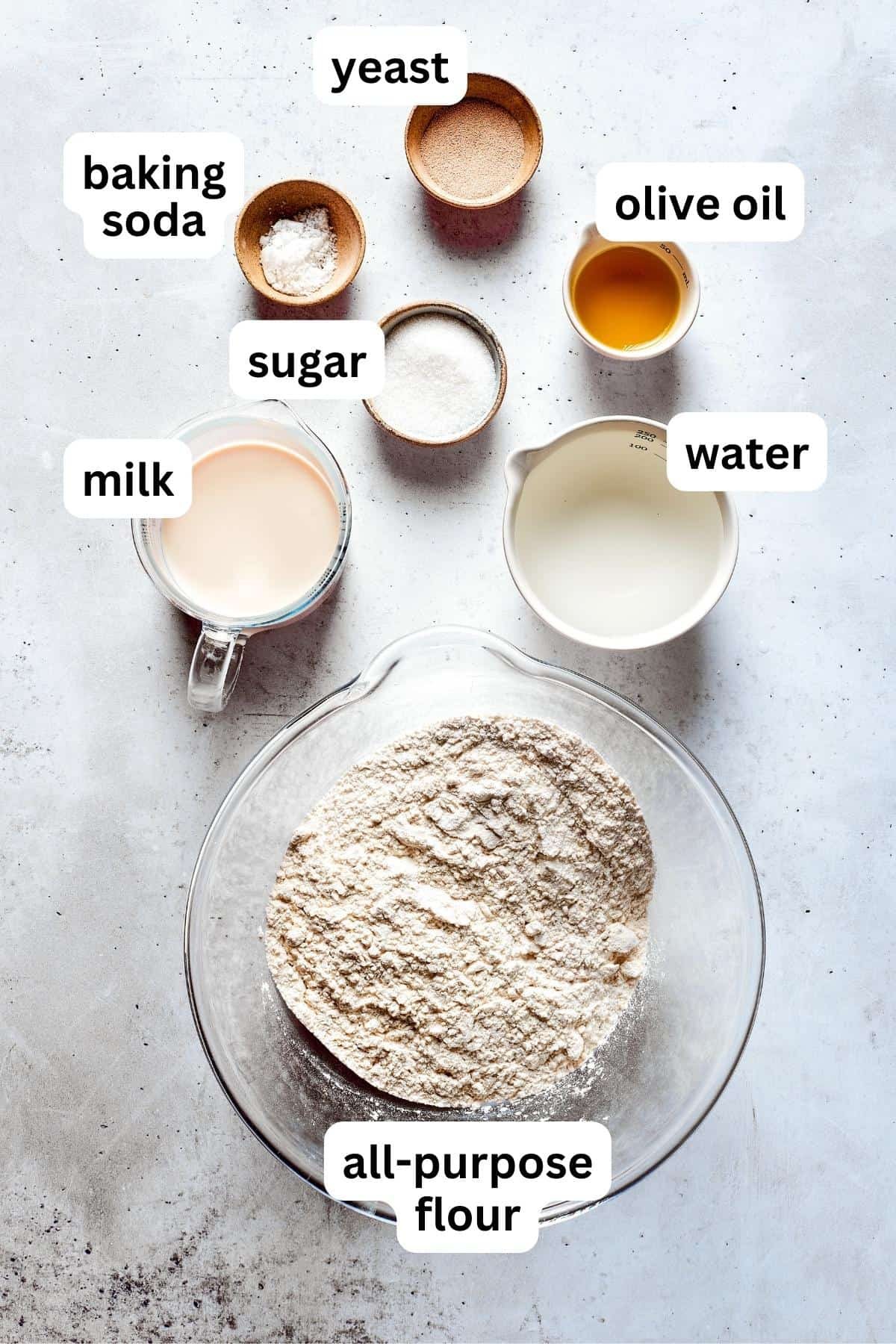 Ingredients for soft pretzels are shown portioned out into bowls: flour, yeast, sugar, milk, butter, and water.