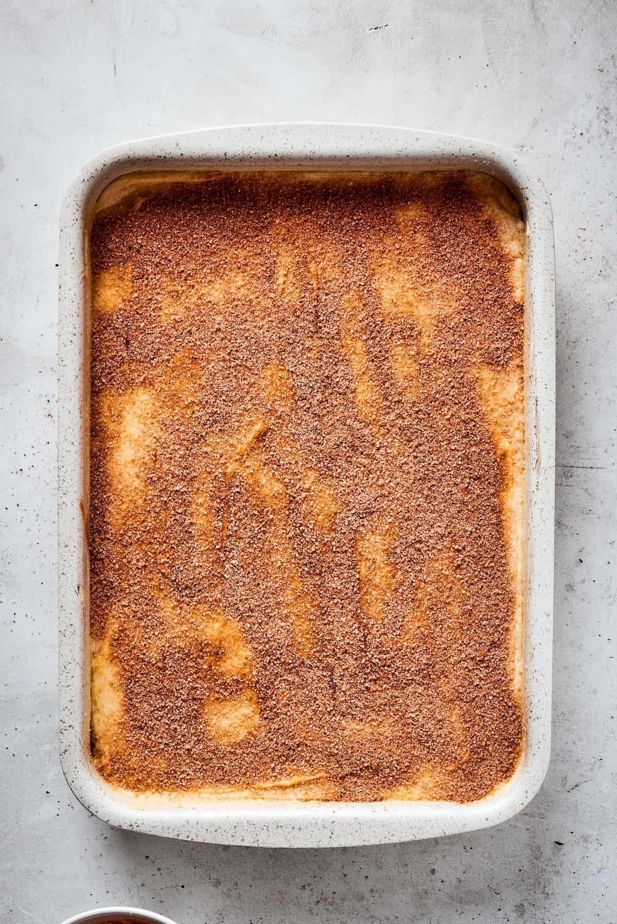 A baking dish with cheesecake filling and crescent roll crusts, topped with butter and cinnamon sugar.